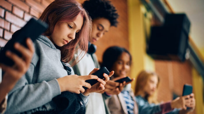 High school student and her friends using their smart phones in a hallway.