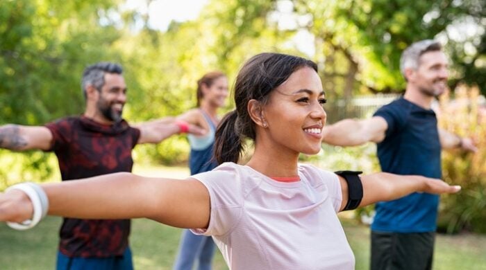 Group of multiethnic mature people stretching arms outdoor. Middle aged yoga class doing breathing exercise at park. Beautifil women and fit men doing breath exercise together with outstretched arms.